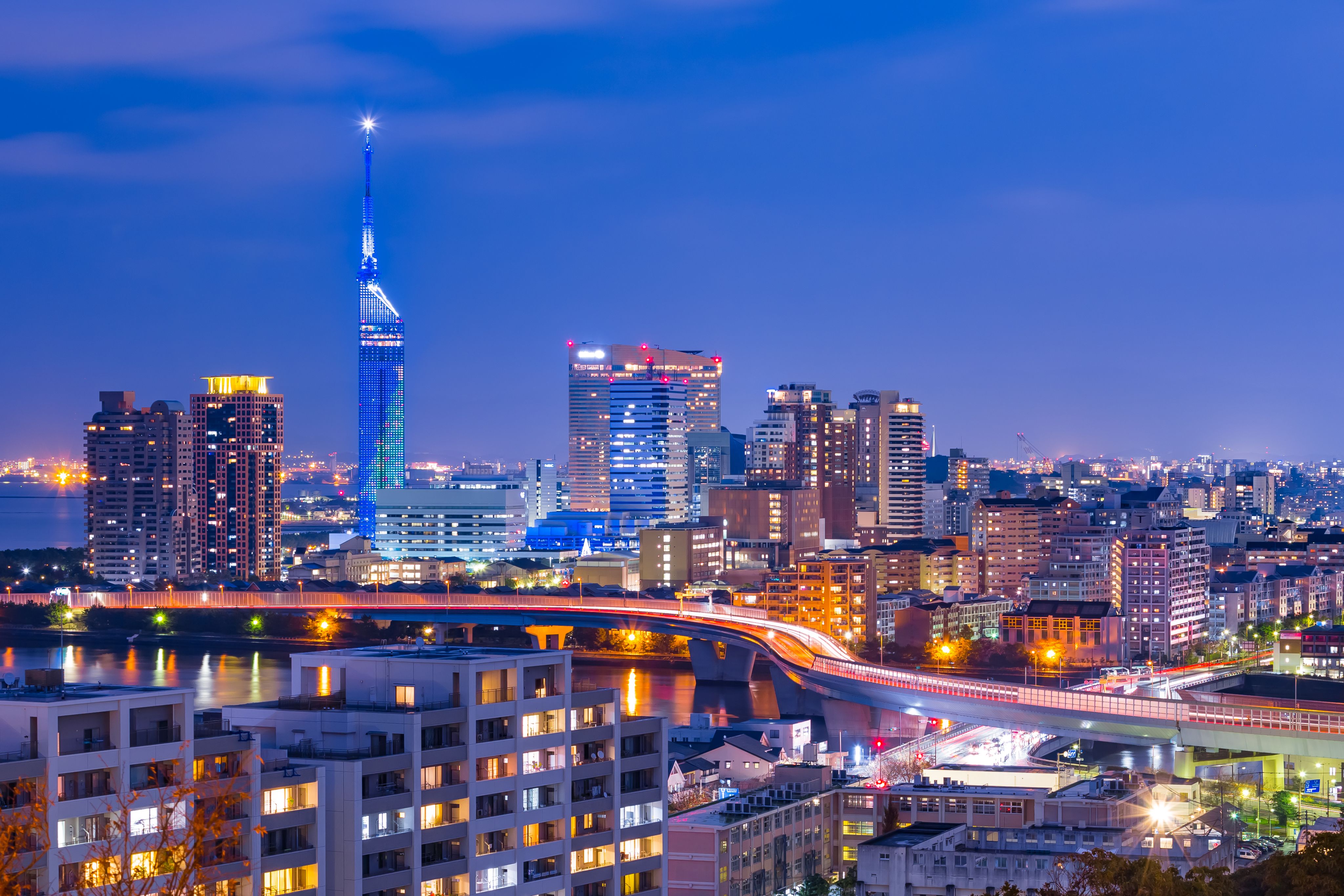 The skyline of Fukuoka at night: tall apartment blocks and a highway across some water.